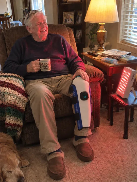 A man seated at home with a knee wrap and a red-light panel